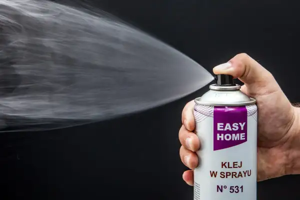 Dłoń trzyma puszkę z napisem "EASY HOME KLEJ W SPRAYU", rozpylając białą mgiełkę. Idealny do podsufitki.
