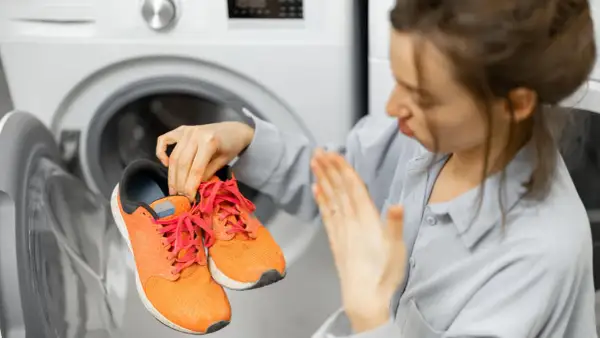 Donna con scarpe arancioni in mano, davanti a una lavatrice aperta. Scopri come lavare le scarpe in lavatrice per farle tornare come nuove.