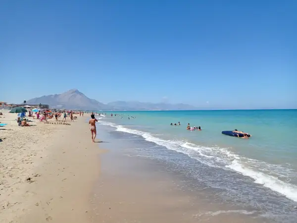 En solig stranddag vid Campofelice di Roccella med folk som badar och kopplar av.
