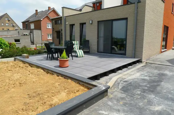 Terrasse en dalles grises sur plots, avec table et chaises, à côté d'un jardin en terre.