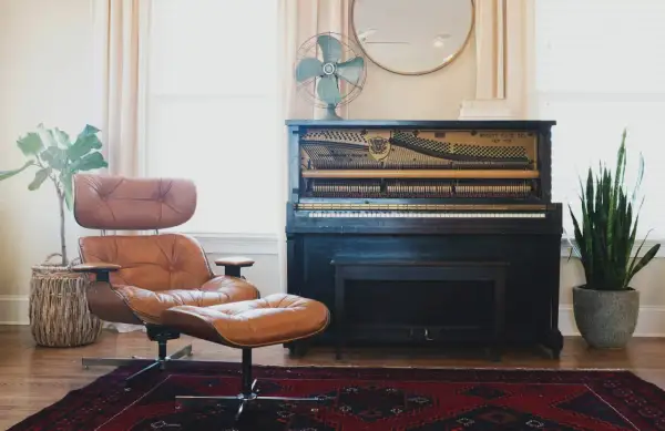 A brown leather armchair and ottoman, a mismatched pair, sit on a Persian rug next to an antique piano.