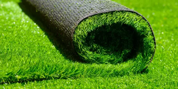 A rolled-up section of artificial grass lies on a bed of lush green turf, hinting at how to install artificial grass for a perfect lawn.