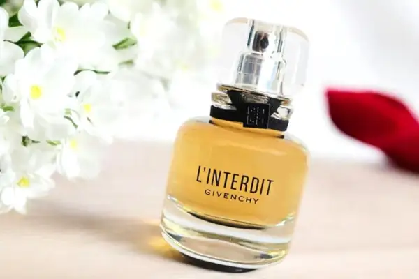 Elegancki flakon perfum L'Interdit Givenchy, otoczony białymi kwiatami i czerwoną szpilką, symbolizuje odwagę i wyrafinowanie.