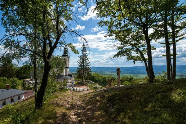 Widok na kościół i krzyż na wzgórzu w **śnieżnicki park krajobrazowy**. W tle rozciąga się malownicza dolina.