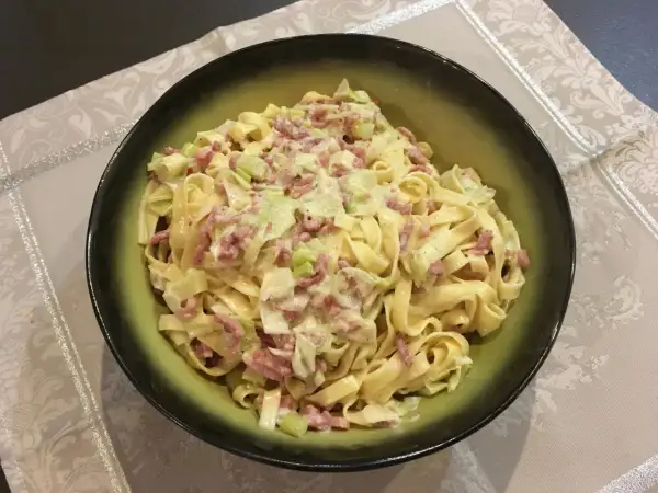 Un plat de tagliatelle poireaux crémeuses avec des lardons, servi dans un bol vert.