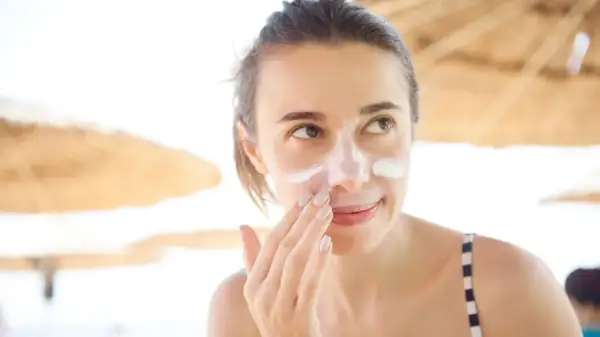 Frau trägt Sonnencreme auf ihr Gesicht auf, um Sonnenbrand zu vermeiden.