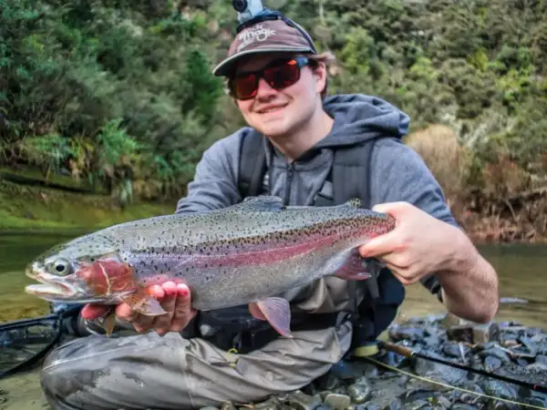 Glad fiske i Ånnaboda! En stolt fiskare håller upp en vacker regnbåge vid en forsande å.