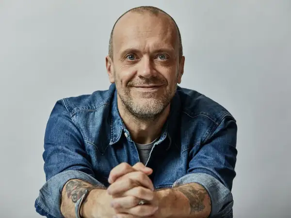 Uomo con barba corta, occhi azzurri, indossa una camicia di jeans. Le sue mani sono intrecciate, eccoti testo.