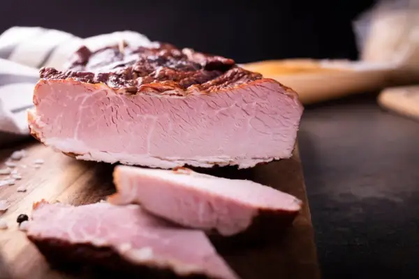 Pokrojona, wędzona szynka na desce. Idealna do przygotowania pysznych kanapek, a jej smak zachwyci każdego, kto lubi wiedzieć, jak parzyć szynkę.