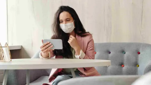 Donna con mascherina guarda il telefono, forse per informarsi sulla situazione, mostrando una certa paura dei virus.