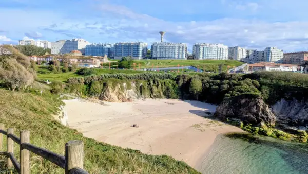 Playa en el parque de bens, con arena dorada, acantilados verdes y edificios modernos al fondo.
