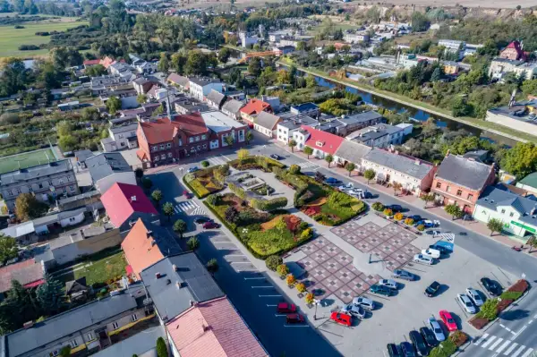 Widok z lotu ptaka na rynek w Barcinie, z kolorowymi rabatami kwiatowymi i brukowanym placem.