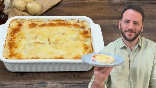 Un uomo sorride mostrando una porzione di parmigiana di patate appena sfornata, dorata e filante.