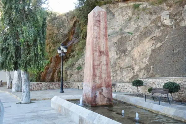 Obelisco en fuente con cascada alhama de almeria al fondo. Árboles y bancos invitan al descanso.