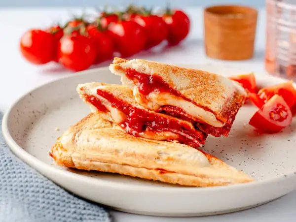 Herzhafte Sandwichmaker Rezepte: goldbraune Sandwiches mit geschmolzenem Käse und Tomatensoße, serviert mit frischen Tomaten.