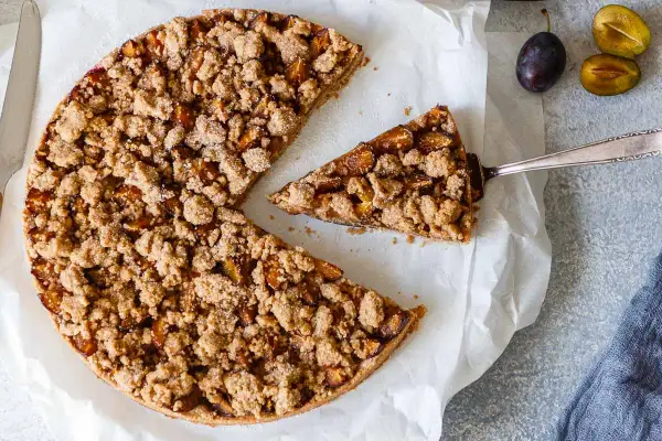 Ein köstlicher, gesunder Pflaumenkuchen mit knuspriger Streuseldecke. Ein Stück wird gerade herausgehoben.