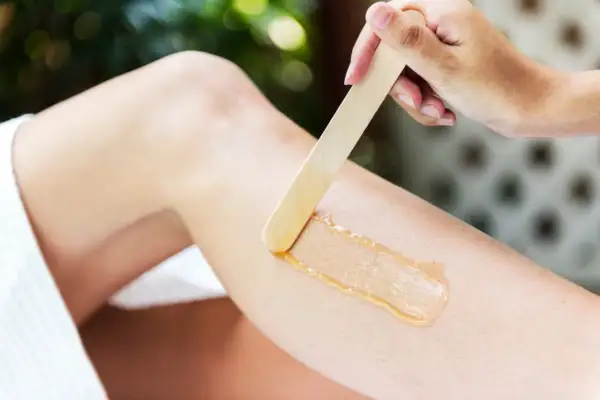 En hand applicerar vax med en träspatel på ett ben för att vaxa bikinilinjen hemma.