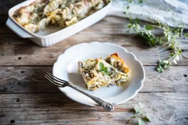 Una fetta di lasagne con carciofi surgelati, guarnita con menta, su un piatto bianco, accanto a una forchetta.
