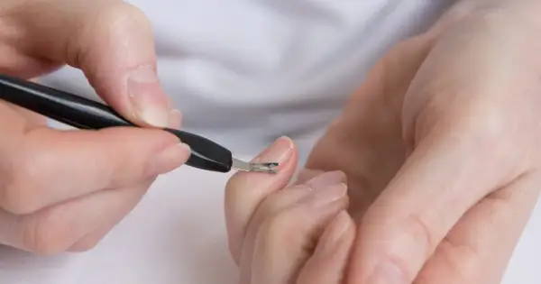 Dłonie podczas zabiegu japońskiego manicure. Narzędzie do usuwania skórek delikatnie pracuje przy paznokciu.