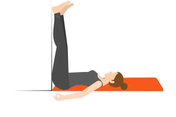 En kvinna stretchar rygg efter gym genom att ligga på en matta med benen uppåt mot en vägg.