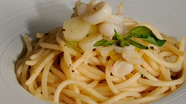 Deliciosos espaguetis con calamares, un plato de pasta con trozos de calamar y hojas verdes, servido en un cuenco blanco.