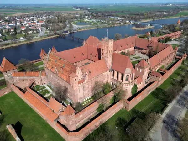 Malbork, największy zamek w Europie, rozciąga się wzdłuż rzeki. Potężne ceglane mury i czerwone dachy tworzą imponujący widok.