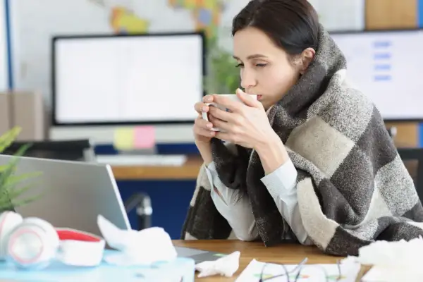 Femme emmitouflée dans une couverture, buvant une tasse de thé, peut-être à cause d'une mauvaise température ambiente.