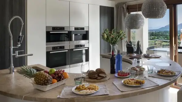 Cocina moderna con encimera curva, electrodomésticos integrados y vista al paisaje. Ideal para un contrato de alquiler temporal, con comida servida y frutas frescas.