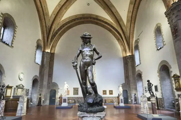Donatello's David, a bronze masterpiece, stands triumphantly in a grand hall, surrounded by other sculptures and art.
