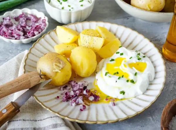 Kartoffeln mit Quark, garniert mit Schnittlauch und verfeinert mit Öl. Dazu gibt es gehackte rote Zwiebeln und ein Messer zum Schälen.