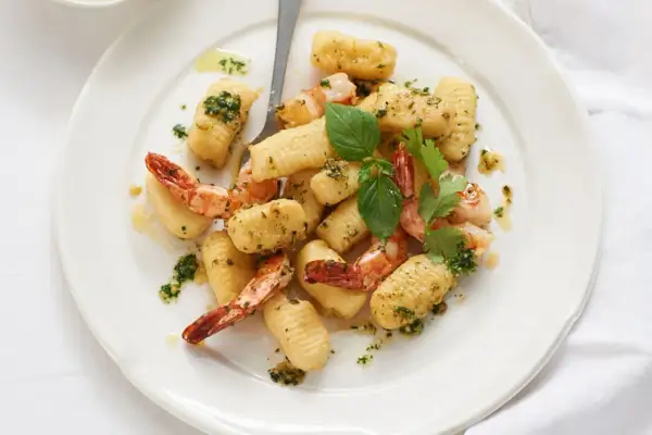 Gnocchi mit Garnelen, verfeinert mit Kräutern und Öl, auf einem weißen Teller angerichtet.