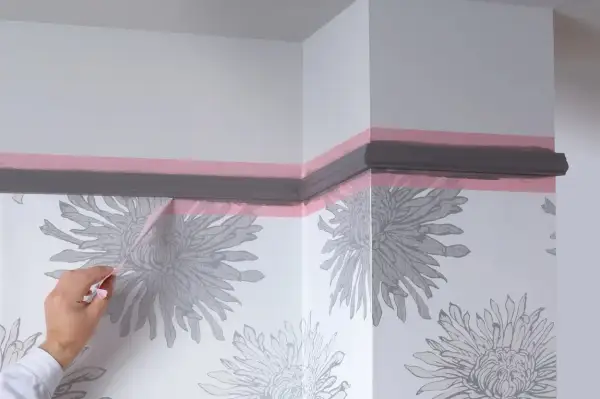 Maintenant, quand enlever bande cache peinture pour une finition parfaite. Un coin de mur avec papier peint à fleurs grises et moulure peinte en gris.