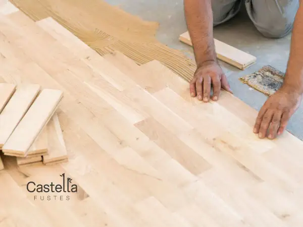 Man installing a light-colored suelo laminado, placing planks on adhesive.