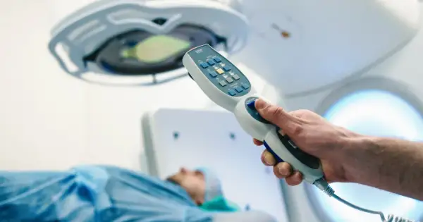 Dłoń trzymająca kontroler aparatu do radioterapii, pacjent na stole. Nowoczesna chemia biologiczna na raka.