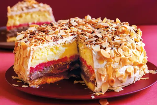 Una fetta di pizza dolce abruzzese, con strati di crema, cioccolato e confettura, ricoperta di mandorle tostate e panna.