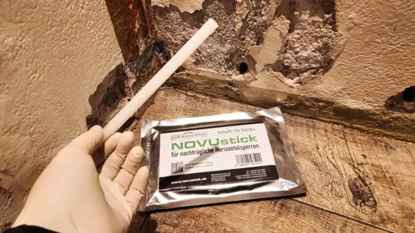 Ein Handschuh hält einen Stab, der für die nachträgliche Horizontalsperre gedacht ist. Das Produkt NOVUstick verspricht, dass man die Horizontalsperre selber machen kann.