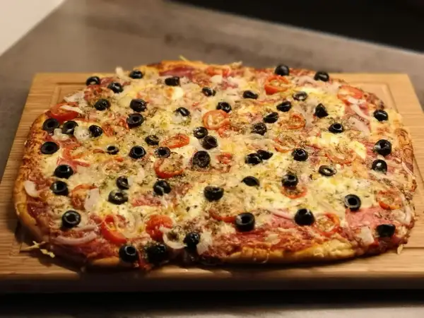 Frisch gebackene Pizza mit Tomaten, Oliven und Käse auf einem Holzbrett. Der Pizzateig wurde im Thermomix zubereitet.
