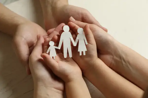 Dłonie dorosłych i dziecka trzymają papierowe figurki rodziny. Symbol wsparcia i troski, jak zasiłek rodzinny.