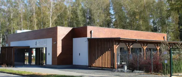 Nowoczesna restauracja Zacisze Ostrzeszów z drewnianą elewacją i przeszklonym wejściem, otoczona drzewami.