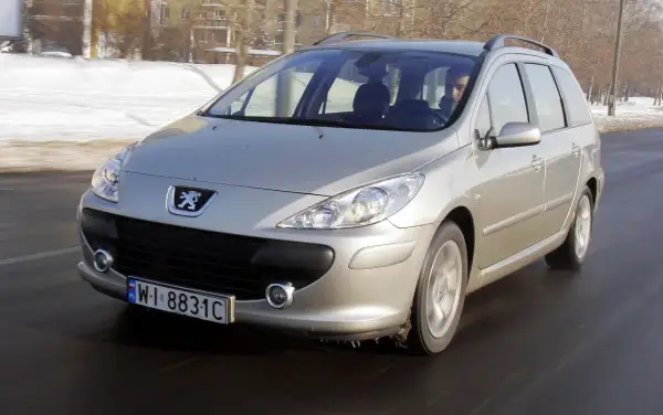 Srebrny Peugeot 307 1.6 HDI w wersji kombi jedzie po drodze, w tle zimowy krajobraz.