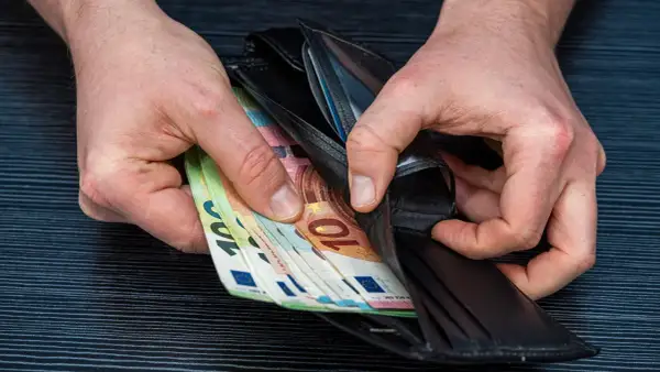 Ręce wkładają euro do portfela. Może to zarobki lakiernika w Niemczech.