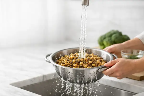 Ceci sono ceci, noti per essere tra i cibi che gonfiano la pancia. Vengono sciacquati sotto l'acqua corrente in una scolapasta.