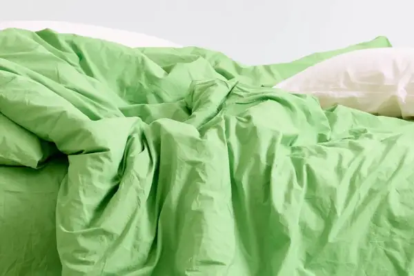 Ein Bett mit zerknitterter, leuchtend grüner Bettwäsche und einem weißen Kissen. Was ist Modal? Es ist ein Stoff, der sich so weich anfühlt.