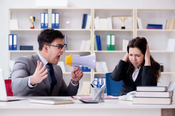 Uomo urla con megafono contro collega che si tappa le orecchie. Un chiaro esempio di **test stress da lavoro**.