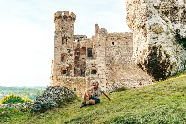 Kobieta odpoczywa na trawiastym zboczu przy ruinach zamku na Szlaku Orlich Gniazd.