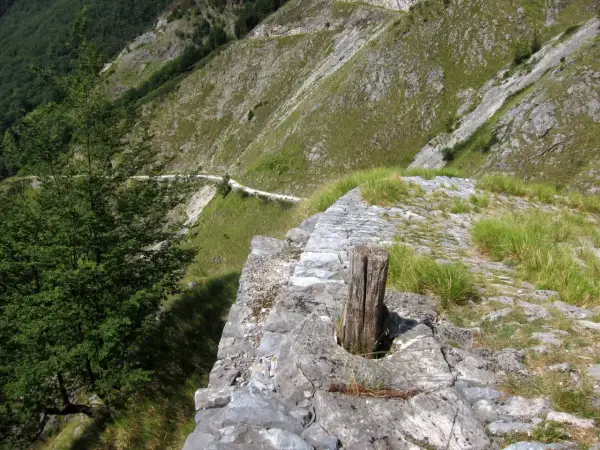 Sentiero lastricato su un versante montuoso, con un tronco di legno che spunta dalla pietra. Un percorso che ricorda le antiche vie, come quelle delle **via Vandelli tappe**.