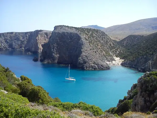 Baia con acque cristalline e una barca a vela. Le scogliere rocciose e la vegetazione mediterranea creano uno scenario suggestivo, perfetto per capire come si misura la profondità del mare.
