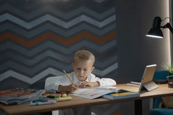 Chłopiec pochyla się nad zeszytem, pisząc ołówkiem. Idealna wysokość biurka dla dziecka zapewnia komfort nauki.
