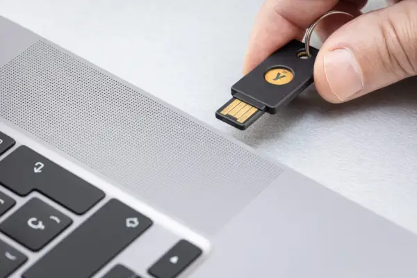 Dłoń zbliża klucz U2F do laptopa. To proste rozwiązanie, które odpowiada na pytanie klucz u2f co to jest – fizyczny klucz do bezpiecznego logowania.