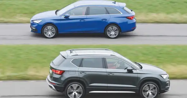 Dwa samochody klasy D: niebieskie kombi i ciemnoszary SUV, jadące obok siebie po drodze.